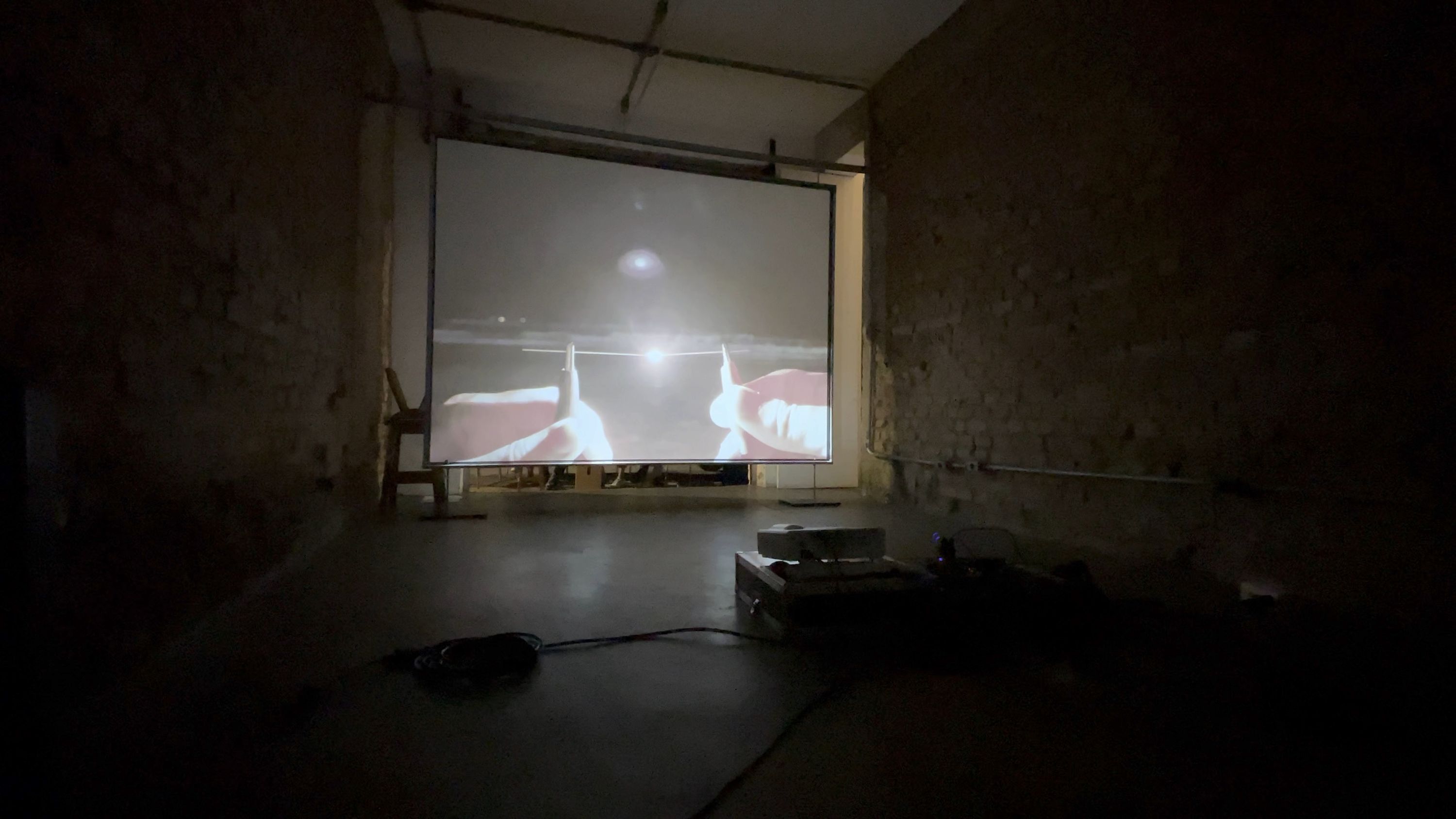 Marissa Lee Benedict and David Rueter, lâmina, 2021, Single-channel video installation, 2:00 TRT, Commissioned for the São Paulo project space um trabalho um texto (one work one text), lâmina is a one-night video work – a singular gesture – exhibited in parallel with a text by curator João Paulo Quintella. Documenting two hands, tentatively, awkwardly, bringing two pieces of 0.7 mm pencil lead (graphite) close enough to spark an electric carbon arc — an early form of spark lighting used for projecting films — before burning out, the work tightly loops together the history of moving image and its means of production.
This tight loop loosens over the course of the evening with a pile-up of strange and unexpected encounters: between the congenial atmosphere of the project space and the passing audience on the street; between the humming fan of a digital projector and the roar of traffic; between the loud squealing kisses of tiny graphite pencil lead rods, powered by a motorcycle battery, burning into light; and between the projected image of a beach at the mouth of a major colonial shipping channel, and the threshold of a garage door.
The exhibition contract for lâmina dictates that this version of the video (not including documentation of the video in situ) will only be publicly shown once (from sunset 18:04:00 to midnight on 26 September 2020 R. Rocha, 386 - Bela Vista, São Paulo, 013300-000, Brazil).
