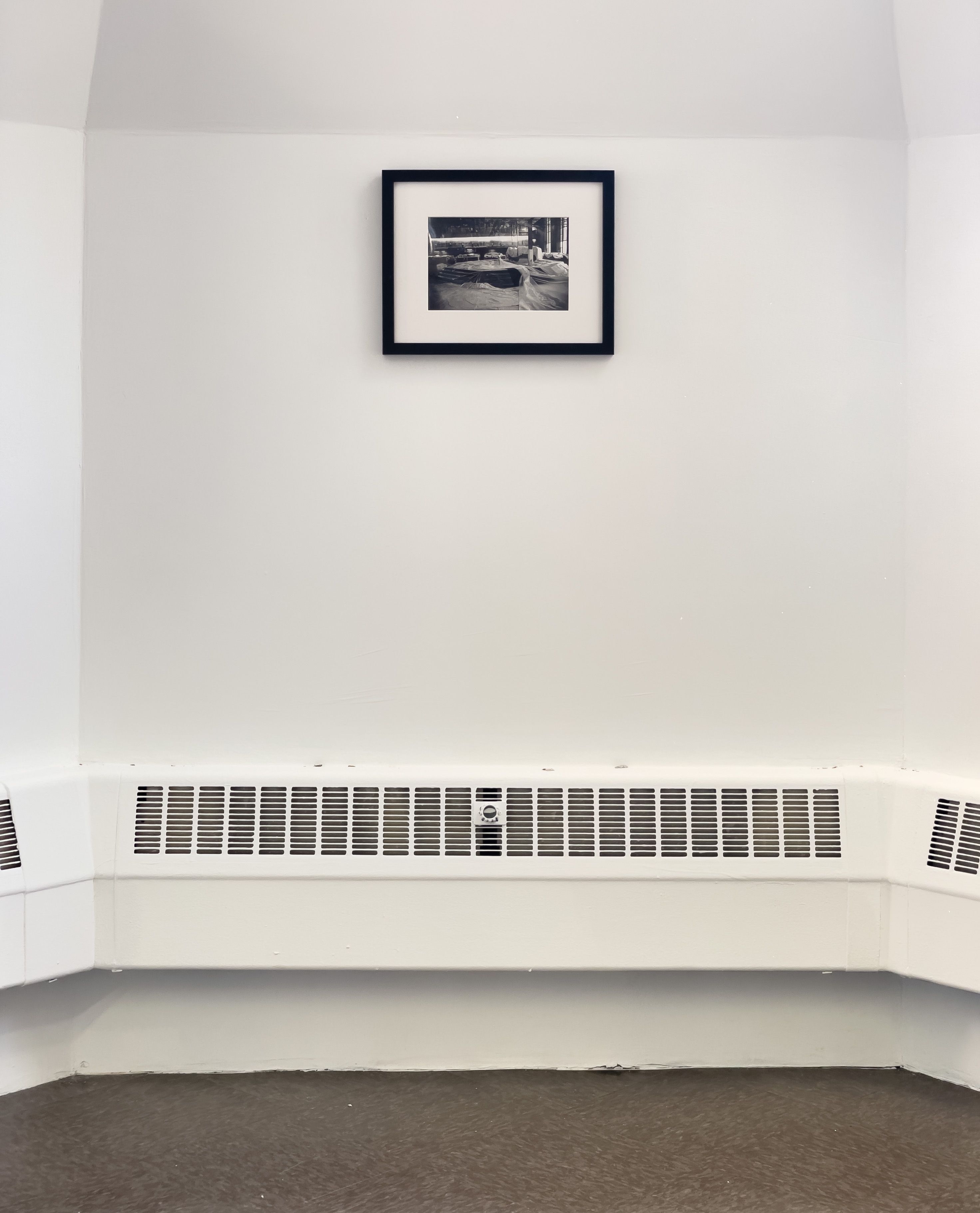 Marissa Lee Benedict, Daniel de Paula, and David Rueter, under cover of a solid object, 2022, Relief in floor wax, excerpt from the artists’ contract for the work deposition (2021), debris removed from ventilation ducts under the Chicago Board of Trade’s former corn futures trading floor, gelatin silver print (circa 1974, photographer unknown; Special Collections and University Archives, University of Illinois, Chicago)., In 2018, Rueter, Benedict, and de Paula acquired a used trading pit from the Chicago Board of Trade, now obsolete as trading goes digital. A huge octagon with seven tiered levels where traders bought and sold corn futures, the pit itself has since traveled to Sao Paolo and back to Chicago. Here it appears only as an outline at full scale, a ghost of itself that questions what can be distilled from a thing’s remnants. A pair of documents and a photograph appear like footnotes above the floor and in the opposite corner of the gallery.